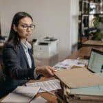 a woman in a suit and glasses holding a file