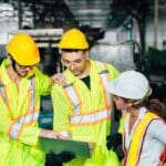 a group of workers in safety vests and hard hats looking at a laptop
