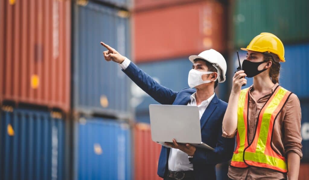 a man in a white hard hat and a mask pointing at a laptop