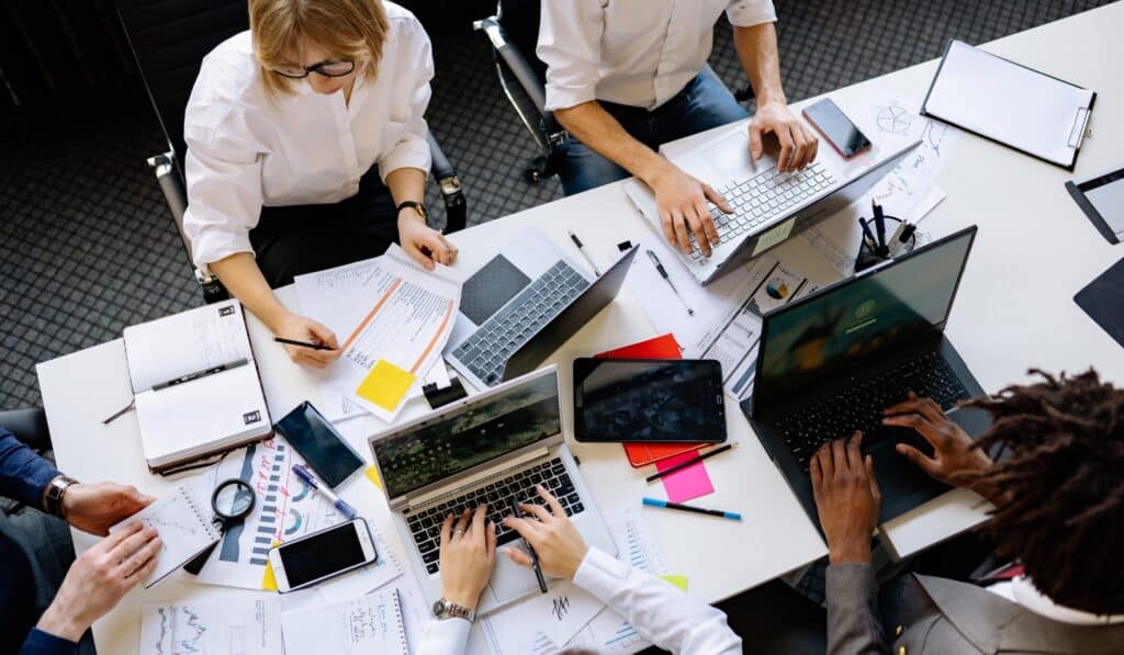 a group of people sitting around a table with laptops and papers